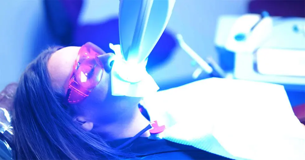 Woman receiving a blue light teeth whitening treatment | Dental whitening equipment used for safe teeth whitening