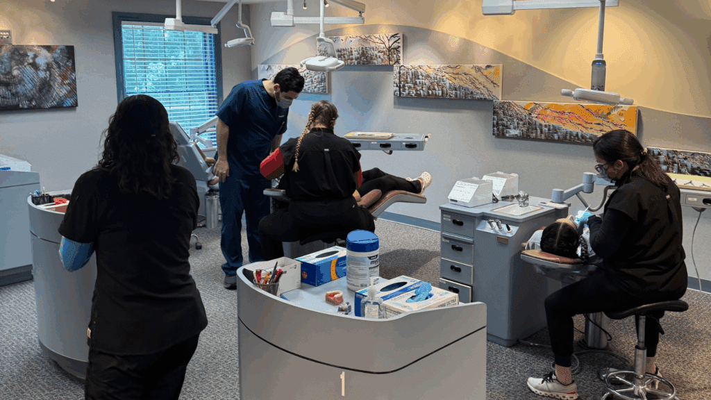 A dental clinic showing three dental professionals attending to patients in separate treatment areas.